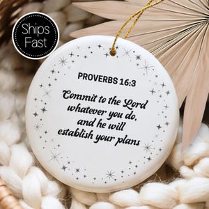 May include: A white ceramic ornament with the text "PROVERBS 16:3" and the quote "Commit to the Lord whatever you do, and he will establish your plans." The ornament has a gold string for hanging and is decorated with small star designs.