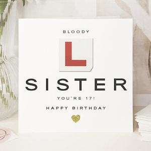 May include: White birthday card with the text "BLOODY SISTER YOU'RE 17! HAPPY BIRTHDAY" and a gold glitter heart. The card features a red and white "L" learner driver sign.
