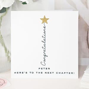 May include: A white card with a gold glitter star and the word "Congratulations" in script. The name "Peter" is below, with the phrase "Here's to the next chapter!" at the bottom. White flowers in a vase are visible in the background.