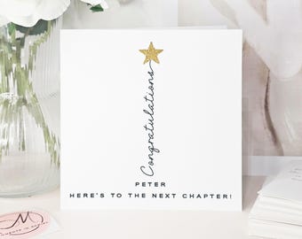 May include: A white card with a gold glitter star and the word "Congratulations" in script. The name "Peter" is below, with the phrase "Here's to the next chapter!" at the bottom. White flowers in a vase are visible in the background.