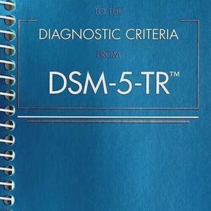 May include: A blue spiral-bound book titled Desk Reference to the Diagnostic Criteria from DSM-5-TR. The cover features white text with horizontal lines above and below the title, and a rectangular border surrounding the diagnostic criteria text.