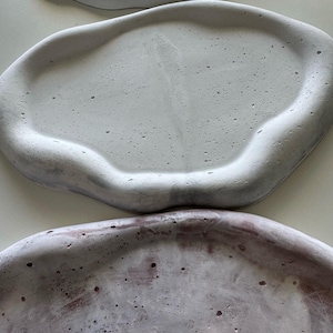 May include: Three white ceramic trays with a textured surface. The trays are different sizes and shapes, with rounded edges. The top tray has a smooth surface, while the bottom two trays have a rougher texture.