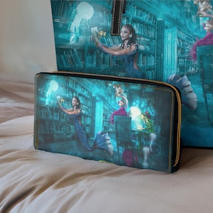 May include: A teal blue zippered wallet with a mermaid and jellyfish design. The mermaid is holding a book and sitting in a library with bookshelves.