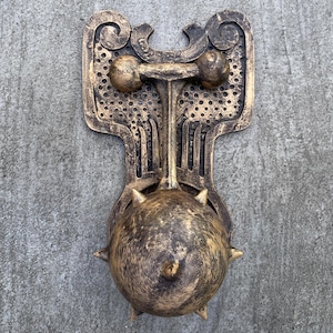 Peut inclure: Un heurtoir de porte en métal doré avec une boule à pointes et un motif décoratif. Le heurtoir est monté sur un mur.