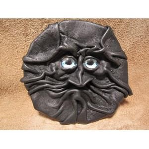 May include: A black leather face sculpture with blue eyes. The face has a wrinkled appearance with a prominent nose and a long, curved mustache. The sculpture is round and appears to be handmade.