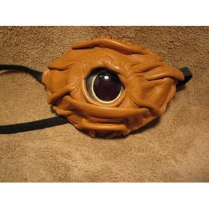May include: A handcrafted, brown leather eye patch with a large, dark red eye-shaped lens. The eye patch has a textured surface and is secured with a black strap. The design is unique and detailed.