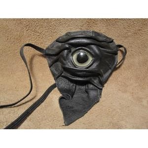 May include: A black leather eye patch with a large, central eye design. The eye patch features a sculpted, textured surface and a strap for securing it. The eye itself is a light color with a dark iris.