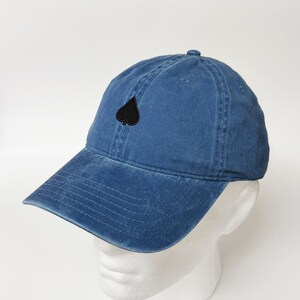 Peut inclure: Une casquette de baseball en denim bleu avec une pique noire brodée sur le devant.