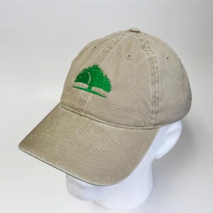 May include: A tan baseball cap with a curved brim. The cap features a green embroidered tree logo on the front. The cap is made of a soft, worn material and has a classic six-panel design.