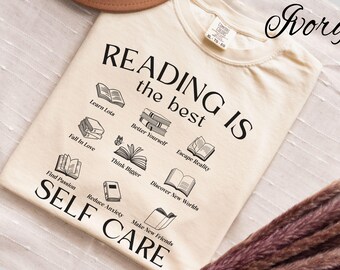 May include: Ivory-coloured t-shirt with the text "READING IS the best SELF CARE" and illustrations of books. The shirt also includes phrases like "Learn Lots," "Fall in Love," and "Reduce Anxiety."