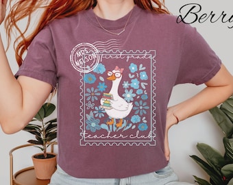 Könnte beinhalten: Beerenfarbenes T-Shirt mit einer skurrilen Gans, die eine Brille und eine Schleife trägt und Bücher hält, in einem Briefmarken-Design. Die Briefmarke enthält den Text "Mrs. Nelson" und "First Grade Teacher Club."