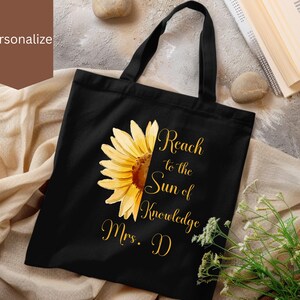 May include: Black tote bag with a sunflower graphic and the text "Reach to the Sun of Knowledge Mrs. D".