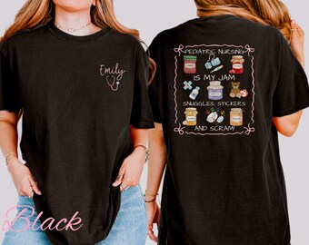 以下が含まれることがあります： 前面に「Emily」の文字と聴診器のグラフィックが入った黒いTシャツ。背面には、「Pediatric Nursing is my Jam, Snuggles, Stickers, and Scram!」の文字と様々なイラストが描かれたデザイン。