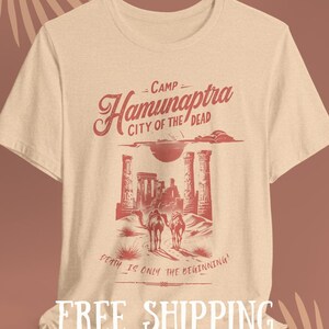 May include: A beige t-shirt with a red graphic design of a desert landscape with the text "Camp Hamunaptra City of the Dead" and "Death is only the beginning!"