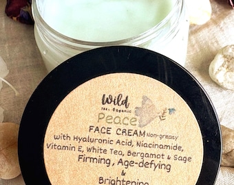 May include: A clear glass jar containing pale green face cream with a black lid. The label reads: Wild Peace FACE CREAM Non-greasy with Hyaluronic Acid, Niacinamide, Vitamin E, White Tea, Bergamot & Sage Firming, Age-defying & Brightening 1 oz | Toxin-free.
