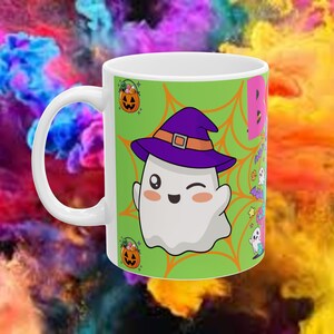 Puede incluir: Taza de cerámica blanca con un diseño temático de Halloween. El diseño presenta un fantasma guiñando un ojo con un sombrero de bruja morado, una calabaza y la palabra "Boo" en rosa. El fondo es un diseño abstracto colorido.