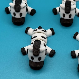 May include: Four small, white and black zebra figurines on a blue background. The zebras are lying on their backs with their legs in the air.