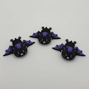 May include: Three black and purple bat-shaped charms with white eyes and a small purple nose.