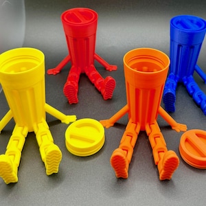 May include: Four colorful, anthropomorphic cup-shaped containers with lids. The cups are yellow, red, orange, and blue. Each has arms, legs, and feet. The lids are the same color as the cups. The cups are on a gray surface.