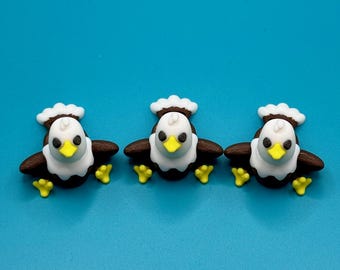May include: Three eagle-shaped decorations with brown wings, white heads, and yellow beaks and feet. Each eagle has a white ruffled collar and a small white tuft on its head. The background is a solid, bright blue.