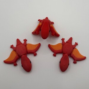 May include: Three red and orange dinosaur toys with wings. The dinosaurs are in different positions, with one facing up, one facing down, and one facing to the side.