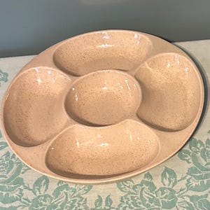 Puede incluir: Una fuente ovalada y moteada con cinco compartimentos. La fuente es de color beige claro con motas más oscuras. Los compartimentos son de varios tamaños y formas, perfectos para servir aperitivos o snacks.