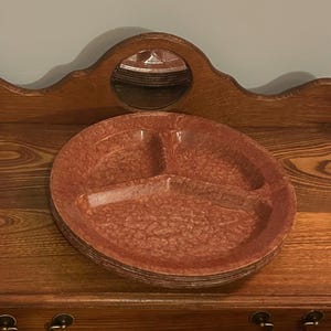 May include: A stack of vintage, oval-shaped serving dishes with three compartments. The dishes are a speckled reddish-brown color and appear to be made of a durable material. They are stacked on a wooden surface, suggesting they are part of a kitchenware collection.