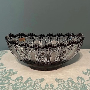 May include: A deep red and clear cut glass bowl featuring an intricate geometric starburst pattern and a scalloped, serrated rim. The bowl has a heavy, faceted base and displays a high-contrast color transition from the dark red upper edge to the clear glass body.