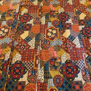 Könnte beinhalten: Ein Stoff mit einem dichten Patchwork-Design aus sich wiederholenden geometrischen und floralen Motiven in den Farben Dunkelrot, Senfgelb, Marineblau und Weiß. Das Muster besteht aus miteinander verbundenen Quadraten und Achtecken mit Details.