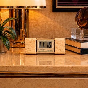 May include: A digital clock with a marble-like design displays the time 11:16. The clock has a gold-colored frame and is flanked by two rectangular blocks. The clock is labeled "Collet" and "Quality times".