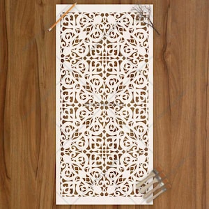 May include: A rectangular white stencil featuring a repeating intricate lattice pattern with symmetrical floral and geometric cutouts. The stencil is positioned alongside a thin orange pencil and a small set of paint brushes with wooden handles.