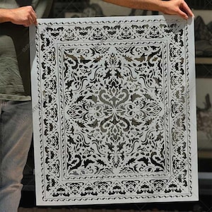 May include: A large, rectangular white stencil sheet featuring a detailed, symmetrical damask-style pattern with intricate floral and scrollwork cutouts. The design includes a wide decorative border surrounding a central ornate motif.