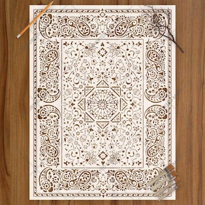 May include: A rectangular stencil sheet featuring a white intricate pattern of paisley motifs, floral elements, and a central geometric medallion. The stencil is positioned on a wood surface with an orange pencil and a small bundle of paint brushes.