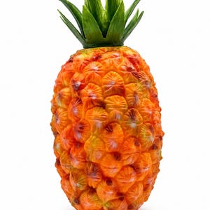 Puede incluir: Una escultura decorativa de piña con un cuerpo naranja vibrante y texturizado, un patrón segmentado repetitivo y una corona de hojas verdes puntiagudas y erguidas en la parte superior. La superficie muestra sutiles variaciones de color.
