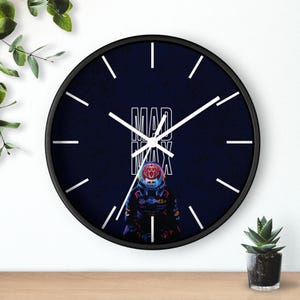 May include: Black round wall clock with white hands and markers. The clock face is dark blue with the words "MAD MAX" in white and a graphic of a race car driver. The clock has a black frame.
