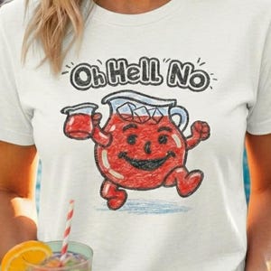 Könnte beinhalten: Weißes T-Shirt mit dem Schriftzug "Oh Hell No" und einem Cartoon-Bild einer roten Krugfigur. Die Person lächelt und hält ein buntes Getränk mit einem Strohhalm.