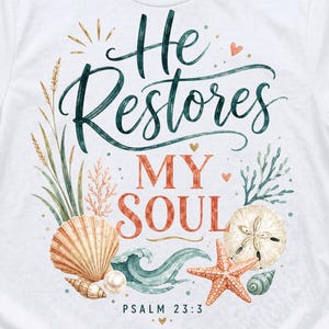 May include: A white t-shirt featuring a graphic design with the text "He Restores MY SOUL" and "PSALM 23:3". The illustration includes watercolor-style seashells, a starfish, a sand dollar, a pearl, sea grass, and a wave in shades of blue, coral, and tan.