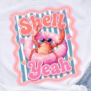May include: White t-shirt featuring a cartoon lobster wearing sunglasses and a pink inflatable ring. The lobster is in the center of the design, with the words "Shell Yeah" in pink and orange lettering.
