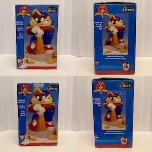 May include: Four boxes of a Looney Tunes cookie jar featuring a cartoon character in a baseball uniform. The jar is blue, red, and yellow. The box reads "Batter Up Cookie Jar" and "Gibson".