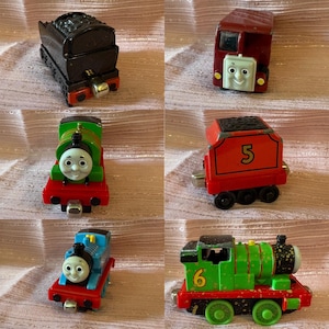 Könnte beinhalten: Eine Sammlung von sechs Spielzeugeisenbahnen aus Druckguss mit verschiedenen Charakteren. Das Set enthält einen schwarzen Kohletender, eine kastanienbraune Lokomotive mit Gesicht, eine grüne Lokomotive mit Gesicht, einen roten Tender mit der Nummer 5, eine blaue Lokomotive und eine grüne Lokomotive mit der Nummer 6.