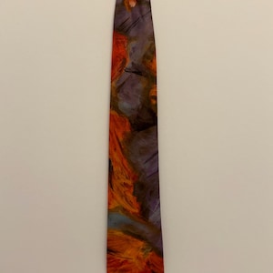 Op de afbeelding: Een stropdas met een abstract ontwerp. De stropdas heeft een mix van kleuren, waaronder oranje, paars en blauw, waardoor een textuurrijk, artistiek uiterlijk ontstaat. De stropdas heeft een standaard lengte en breedte, geschikt voor formele of semi-formele gelegenheden.