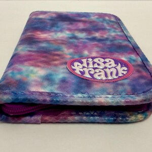 May include: A rectangular, zippered pencil case with a tie-dye pattern in shades of blue, purple, and pink. The case features the text "Elisa Frank" on a pink oval patch. The zipper is a deep purple color.
