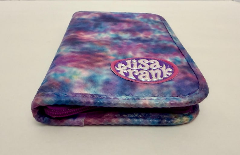 May include: A rectangular, zippered pencil case with a tie-dye pattern in shades of blue, purple, and pink. The case features the text "Elisa Frank" on a pink oval patch. The zipper is a deep purple color.