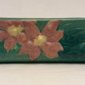 May include: A rectangular, green ceramic planter with two handles and a floral design. The flowers are a muted red with yellow centers. The planter is approximately 25 cm long.