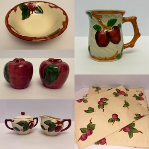 Op de afbeelding: Een collectie keramisch keukengerei met appelmotieven, waaronder een kom, een mok met mandvlechtstructuur, twee appelvormige strooiers, een suikerpot met deksel, een melkkannetje en crèmekleurige stoffen placemats met een appelprint.