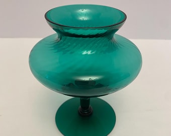 Puede incluir: Un jarrón de vidrio verde azulado con una base ancha y un cuello estrecho. El jarrón tiene un diseño de espiral y se asienta sobre una base circular.