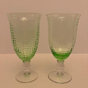 Könnte beinhalten: Zwei grün getönte, strukturierte Glasbecher. Die Becher haben ein strukturiertes Muster auf der Schale und einen klaren Stiel und Boden. Der Boden ist rund und flach. Die Becher sind leer und stehen auf einer weißen Oberfläche.