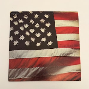 May include: A square vinyl record jacket featuring a graphic of an American flag with a black canton containing white, multi-pointed star-like shapes instead of traditional stars. The text STEREO/KE 30986 is printed in the upper left corner.
