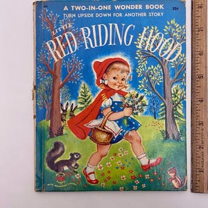 Peut inclure: Couverture de livre pour enfants vintage "Little Red Riding Hood". L'illustration montre une fillette en cape et capuche rouge, tenant un panier et des fleurs. Le fond est un ciel bleu avec des arbres et des animaux. Le livre mesure 15 cm de haut.