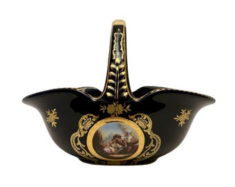 May include: A dark blue ceramic basket with a handle, adorned with gold floral patterns and a central oval painting. The handle and rim are accented with gold trim. The basket's design is ornate and elegant.